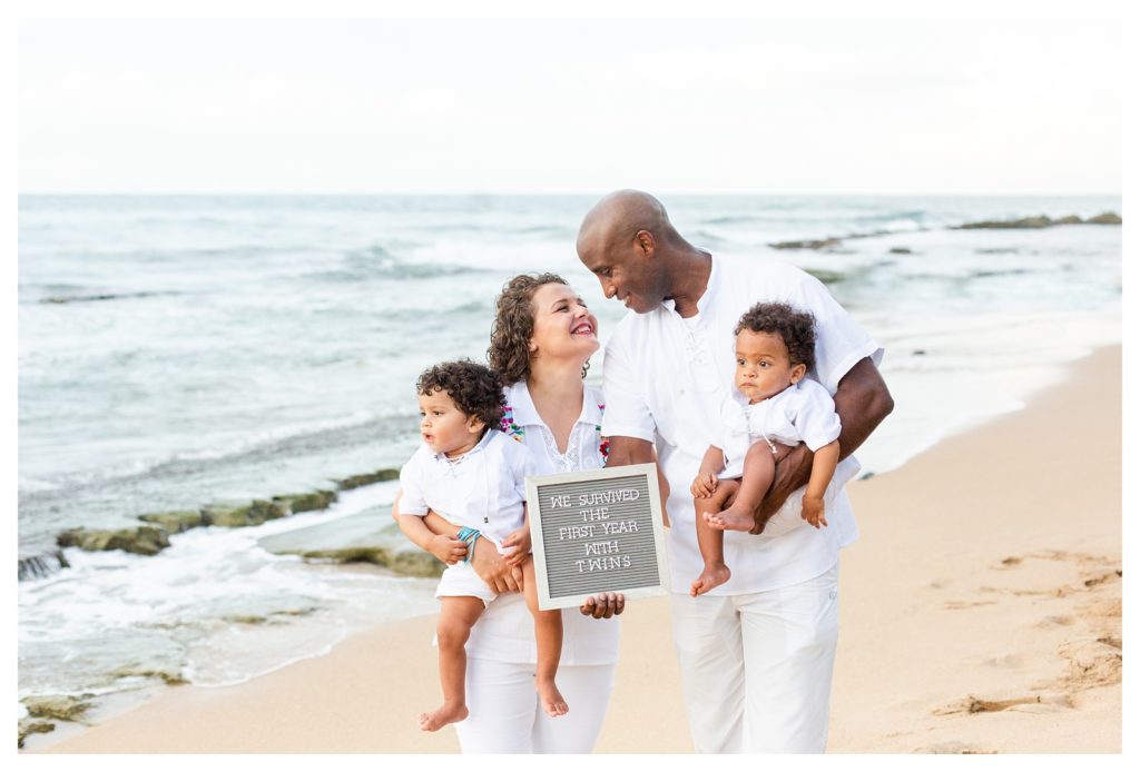 Family Session with twins at Condado Beach holding sign that says, "We survived the first year with twins."