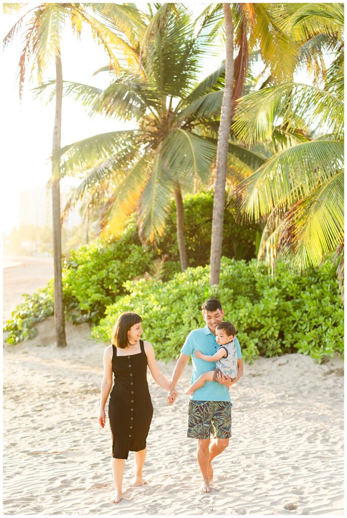 Image of a family beach photo session in Isla Verde, Puerto Rico. Family of three walking in the sand with palm trees in the background.